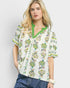 Woman wearing a floral blouse with green trim on a plain background