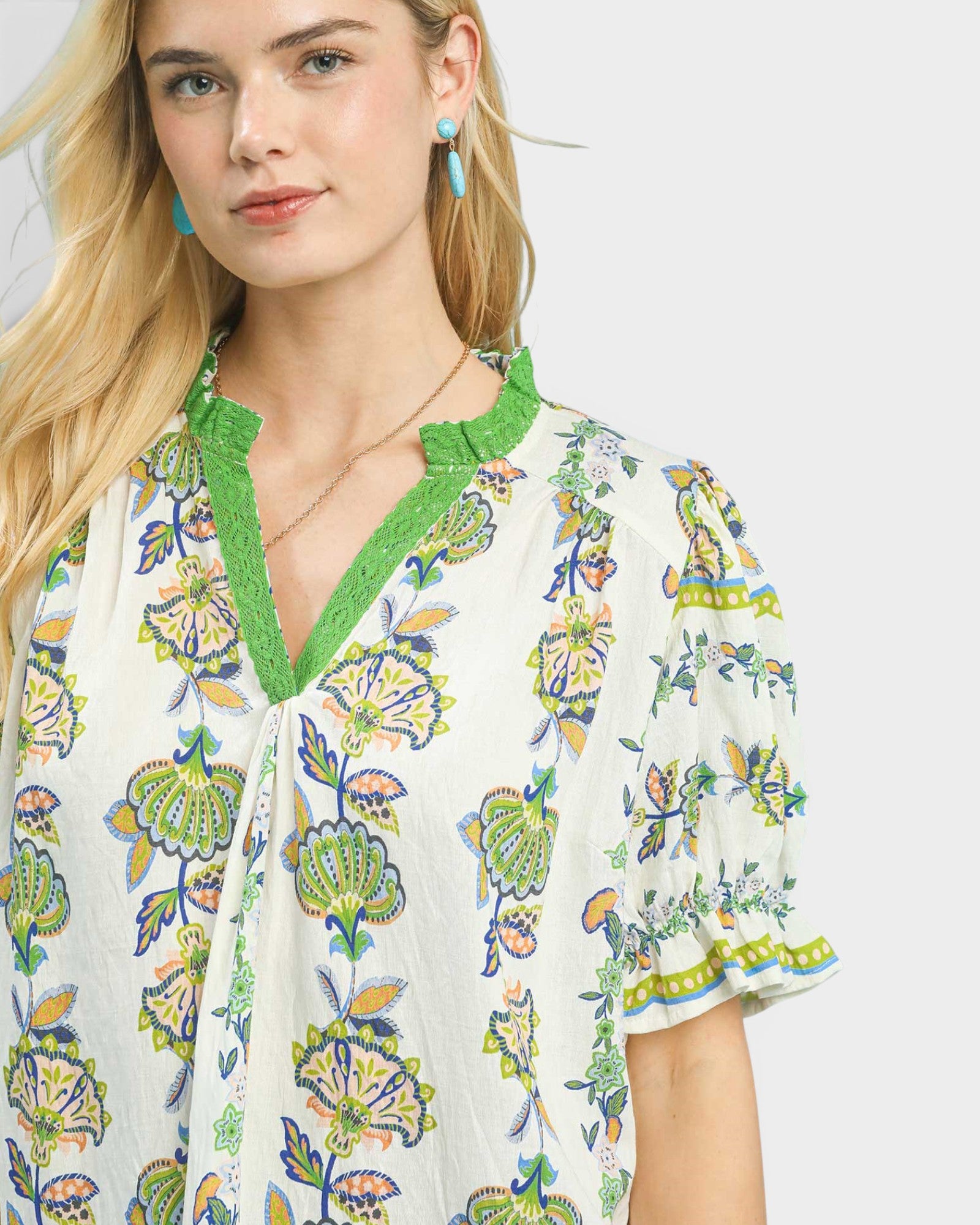 Woman wearing a floral blouse with green trim on a white background