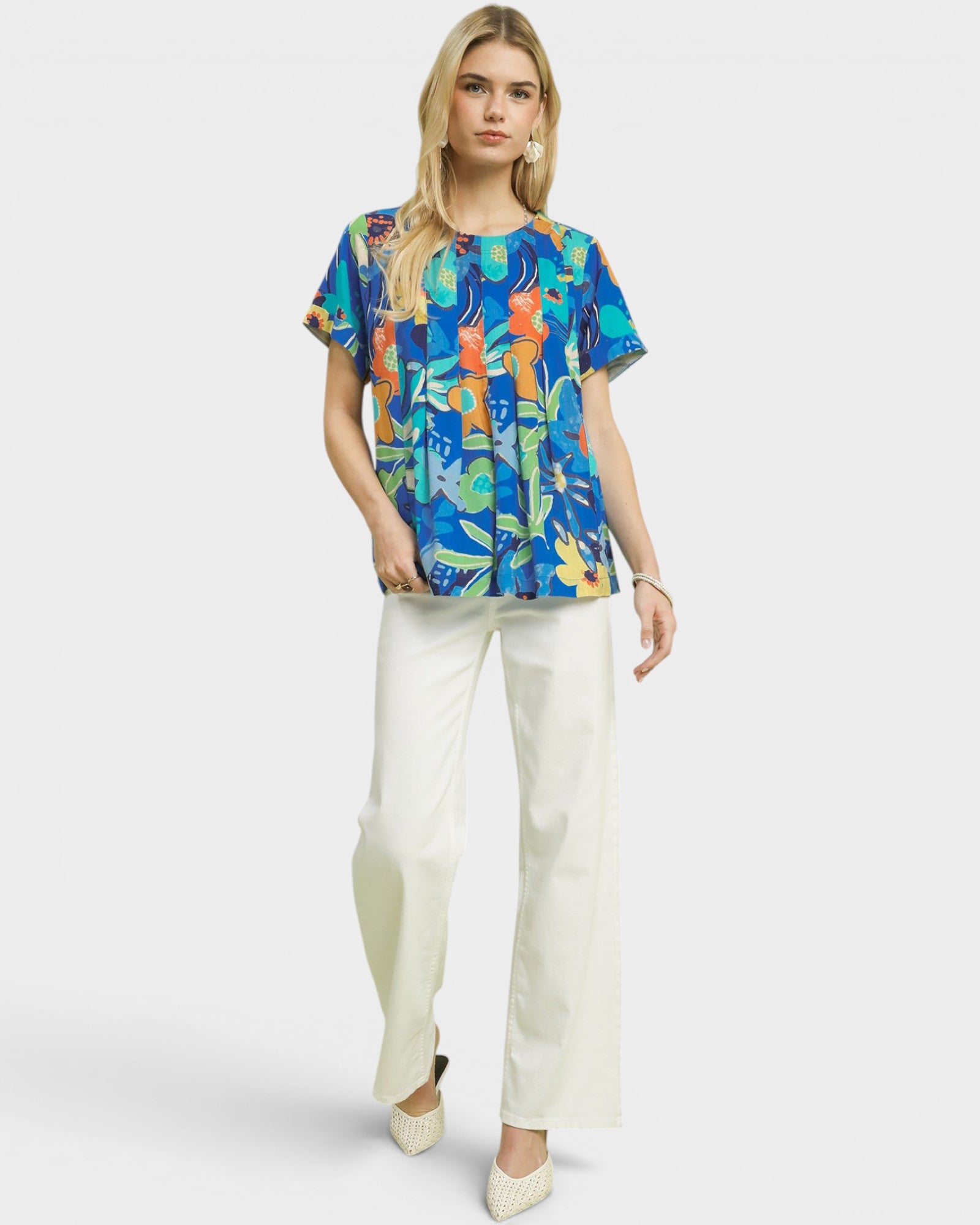 Woman wearing a colorful patterned top and white pants on a white background