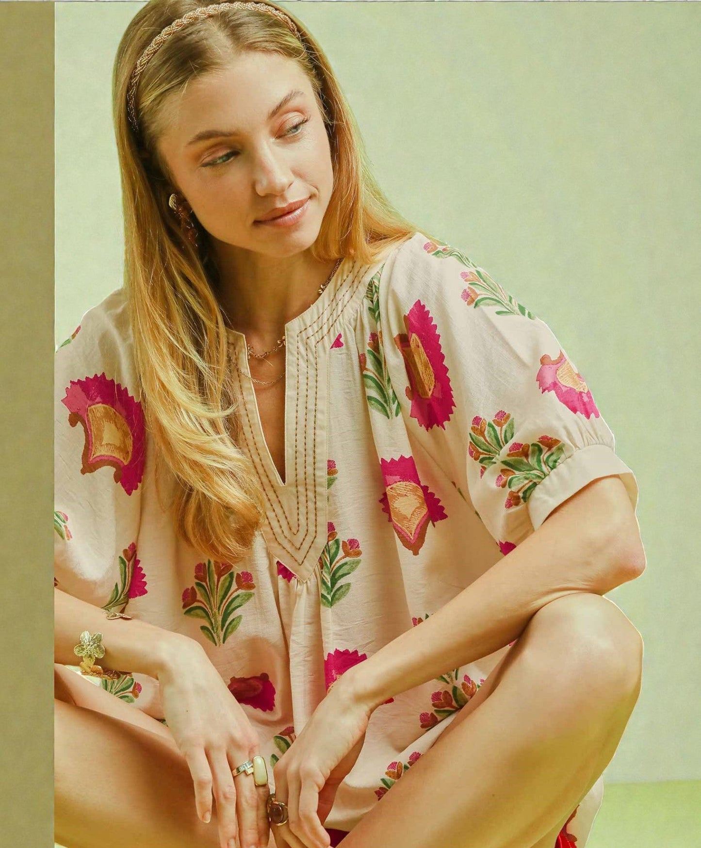 Woman wearing a floral dress sitting on the ground against a light green background