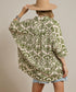 Person wearing a green and beige patterned shirt with a beige hat on a plain background