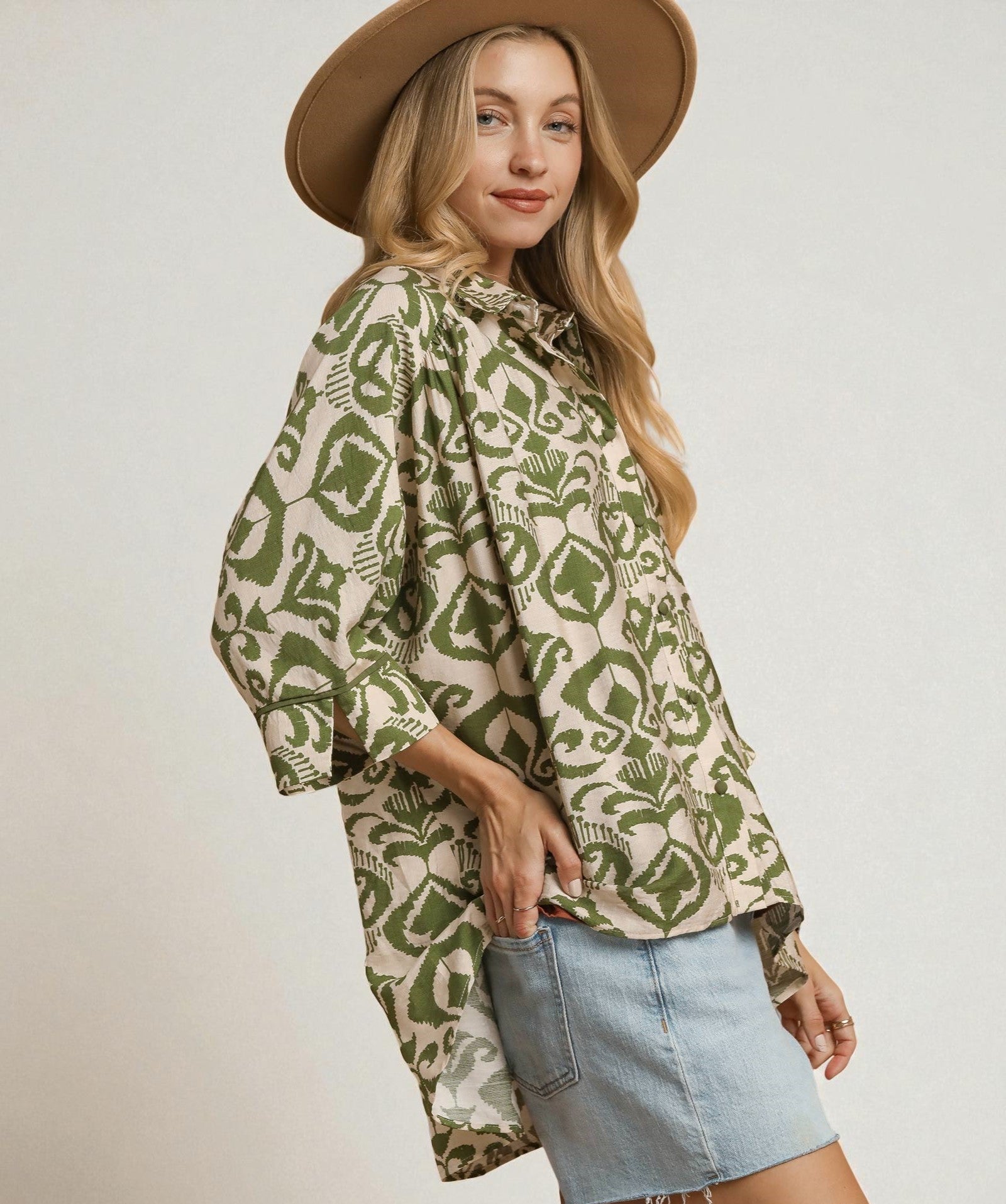 Woman wearing a patterned shirt and denim skirt with a beige hat on a plain background