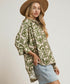Woman wearing a patterned shirt and denim skirt with a beige hat on a plain background