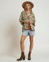 Woman wearing a patterned shirt, denim shorts, and brown boots on a plain background
