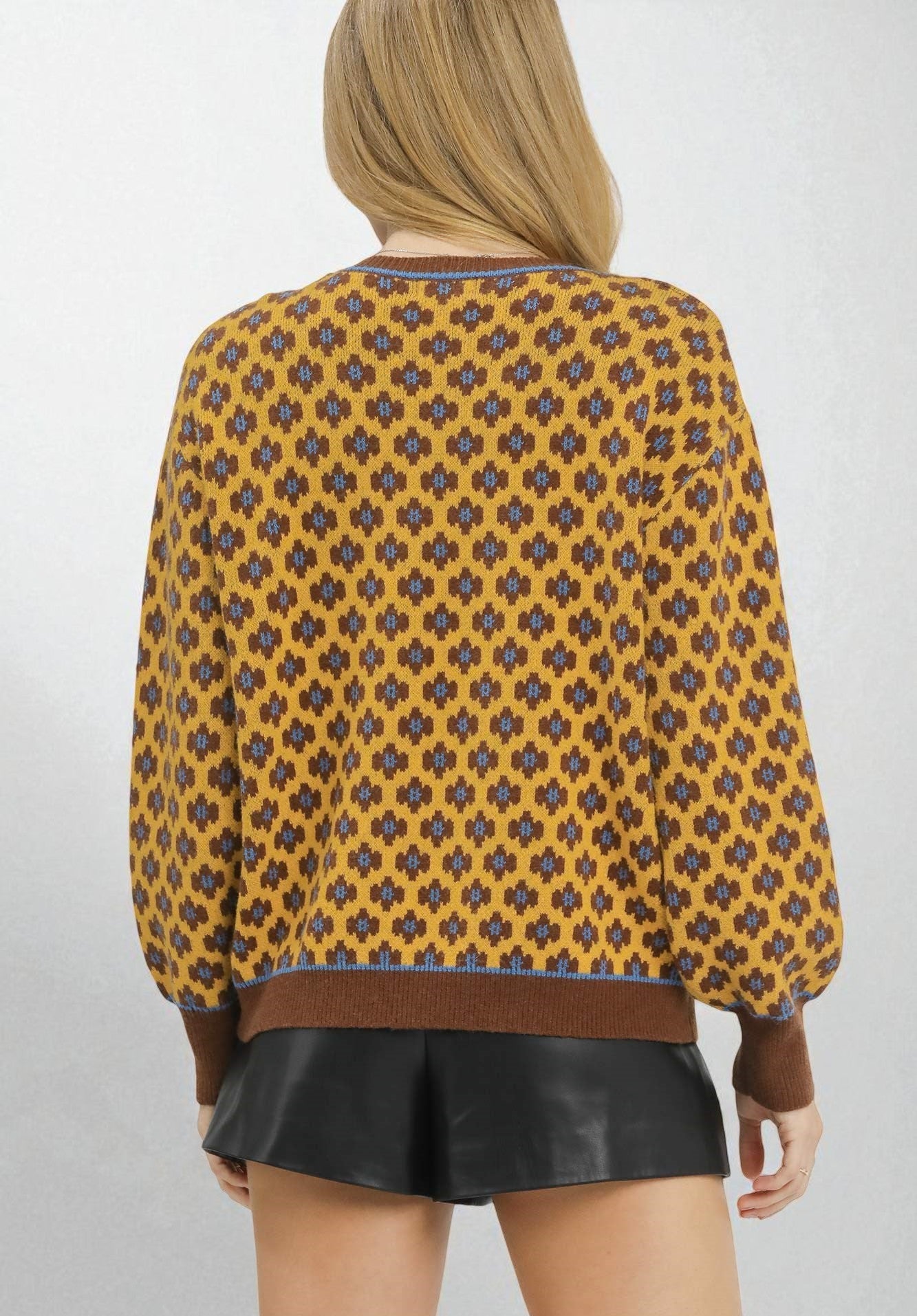 Person wearing a patterned yellow and brown top with a plain background