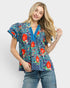 Woman wearing a colorful patterned blouse with red floral designs on a white background