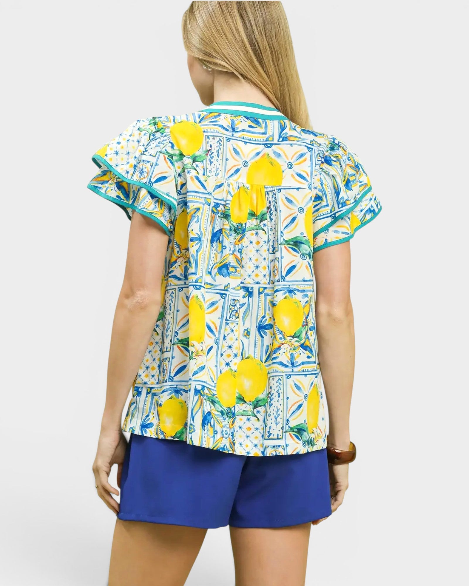 Woman wearing a colorful blouse with lemon pattern and blue shorts on a white background