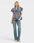 Woman wearing a colorful patterned blouse and blue jeans on a white background