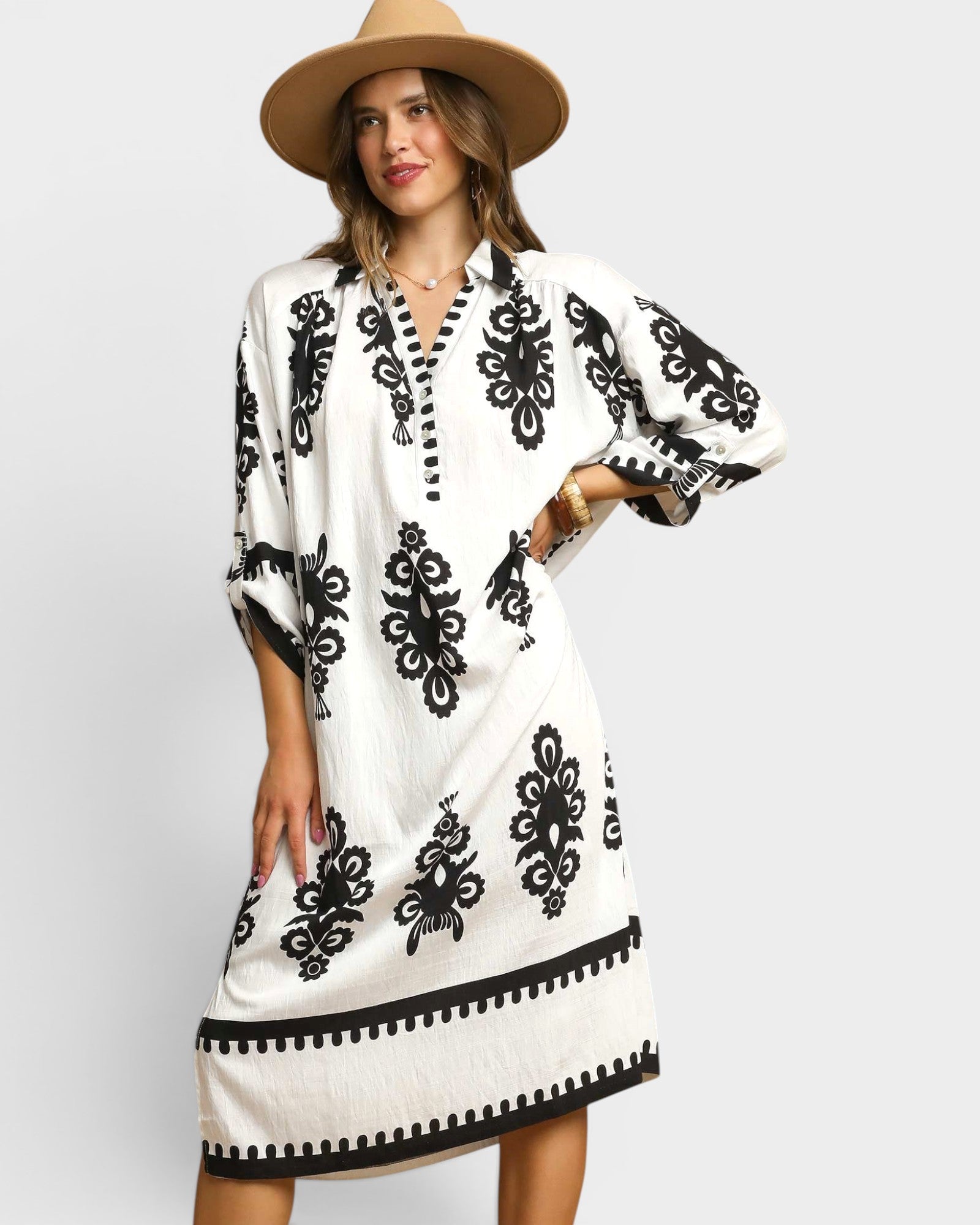 Woman wearing a white dress with black patterns and a beige hat on a light gray background