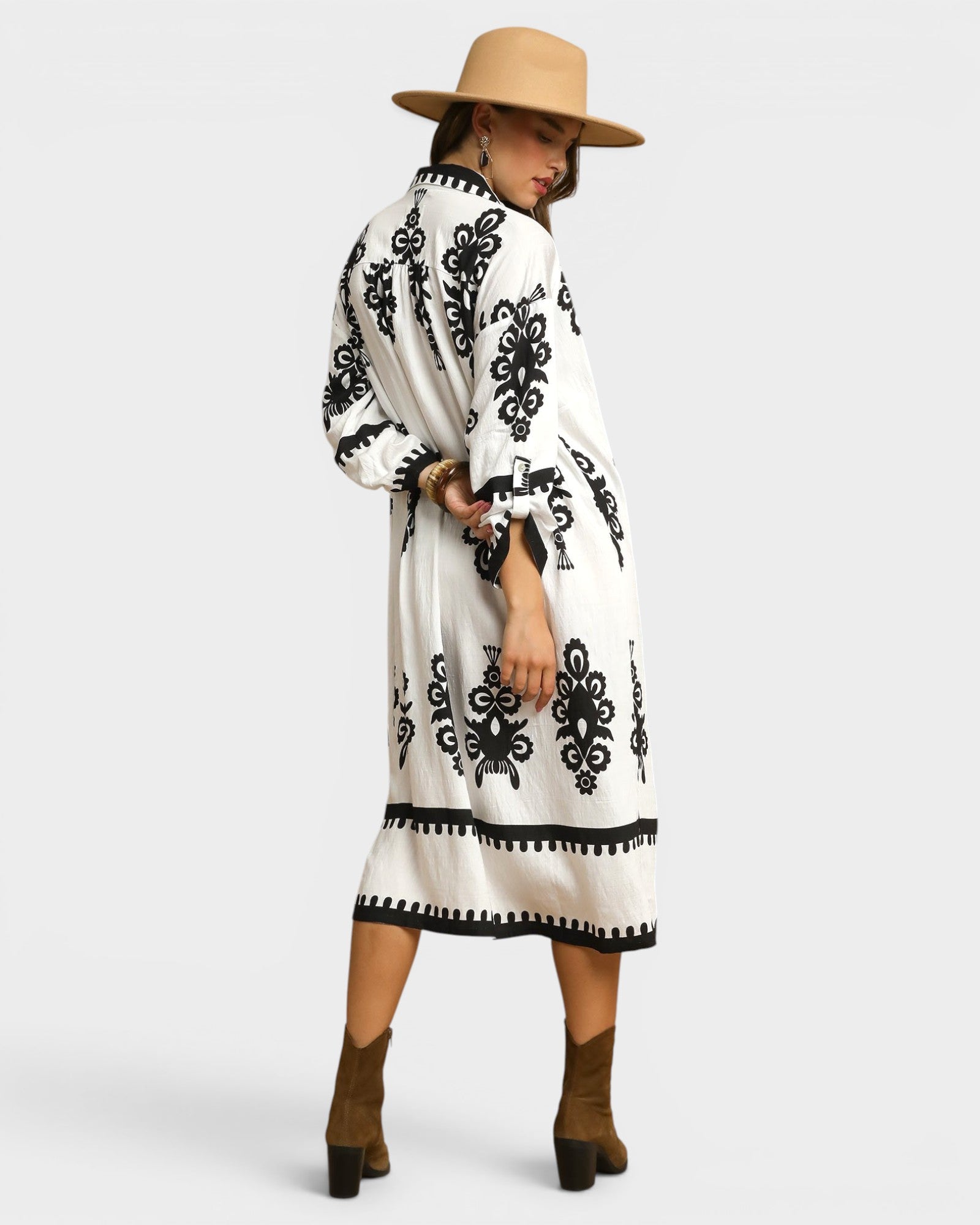 Woman wearing a white dress with black patterns and a beige hat on a white background