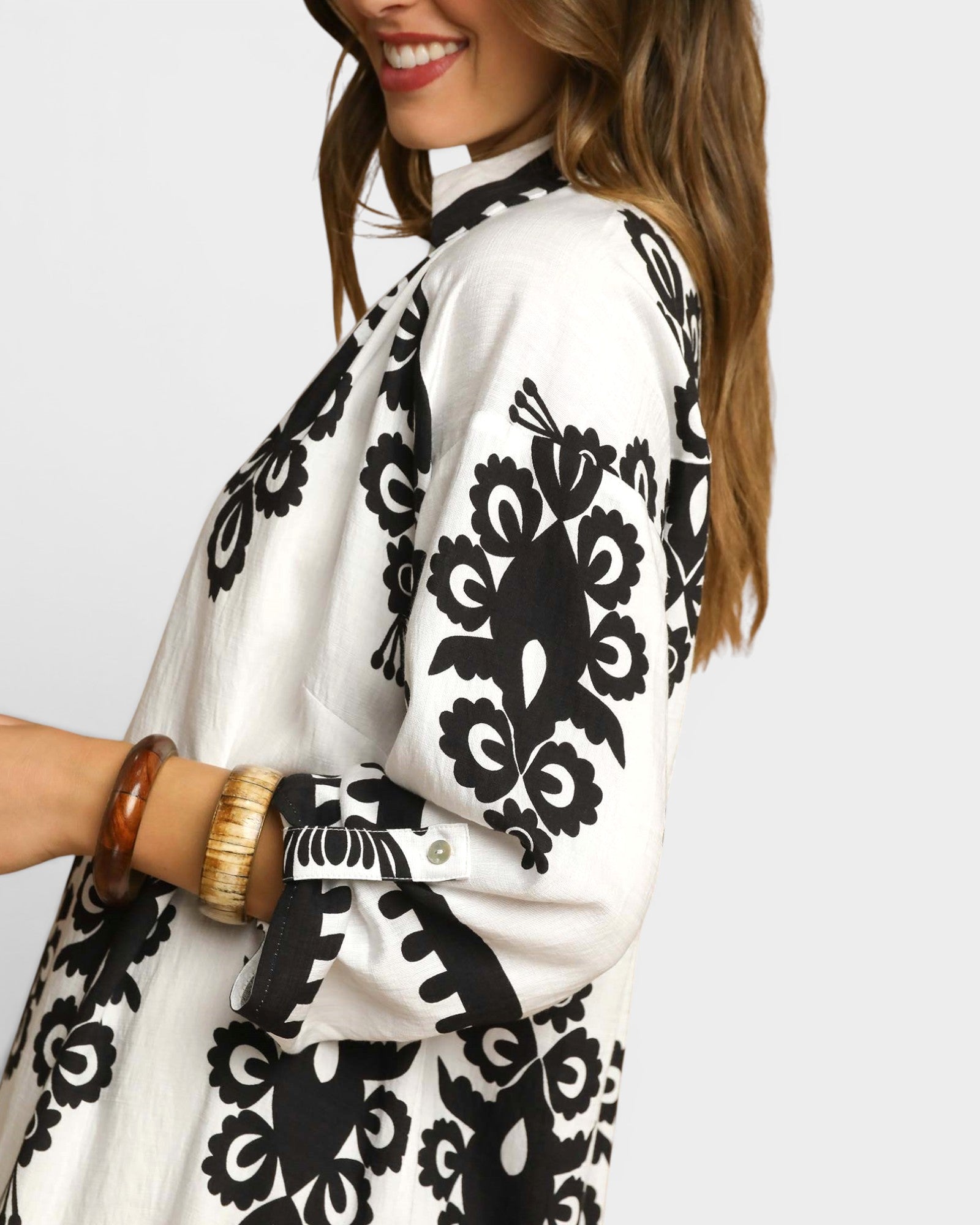 Woman wearing a white blouse with black floral patterns on a plain background