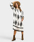 Woman wearing a white dress with black patterns, brown boots, and a beige hat on a white background