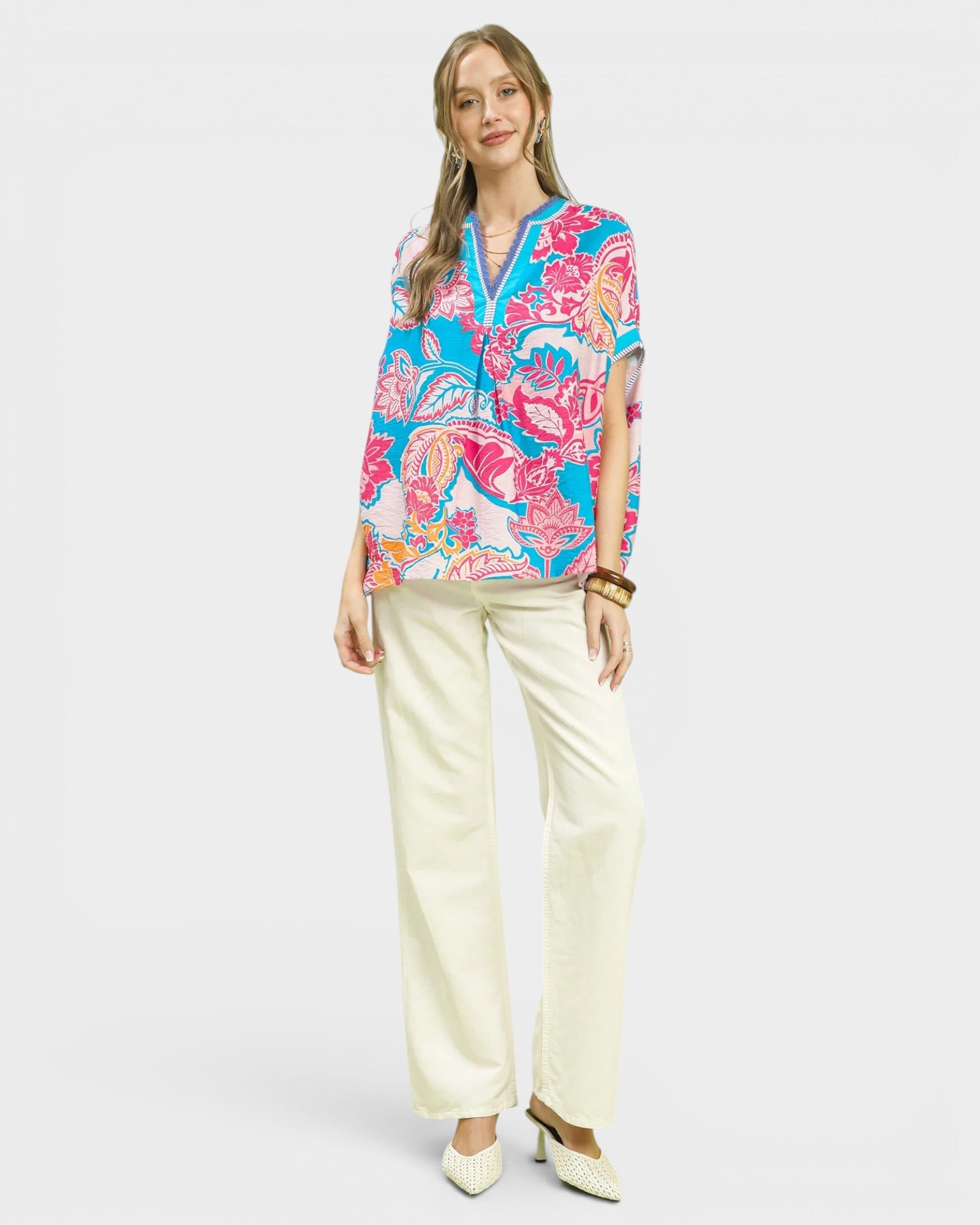 Woman wearing a colorful patterned blouse and white pants on a white background
