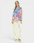 Woman wearing a colorful patterned blouse and white pants on a white background