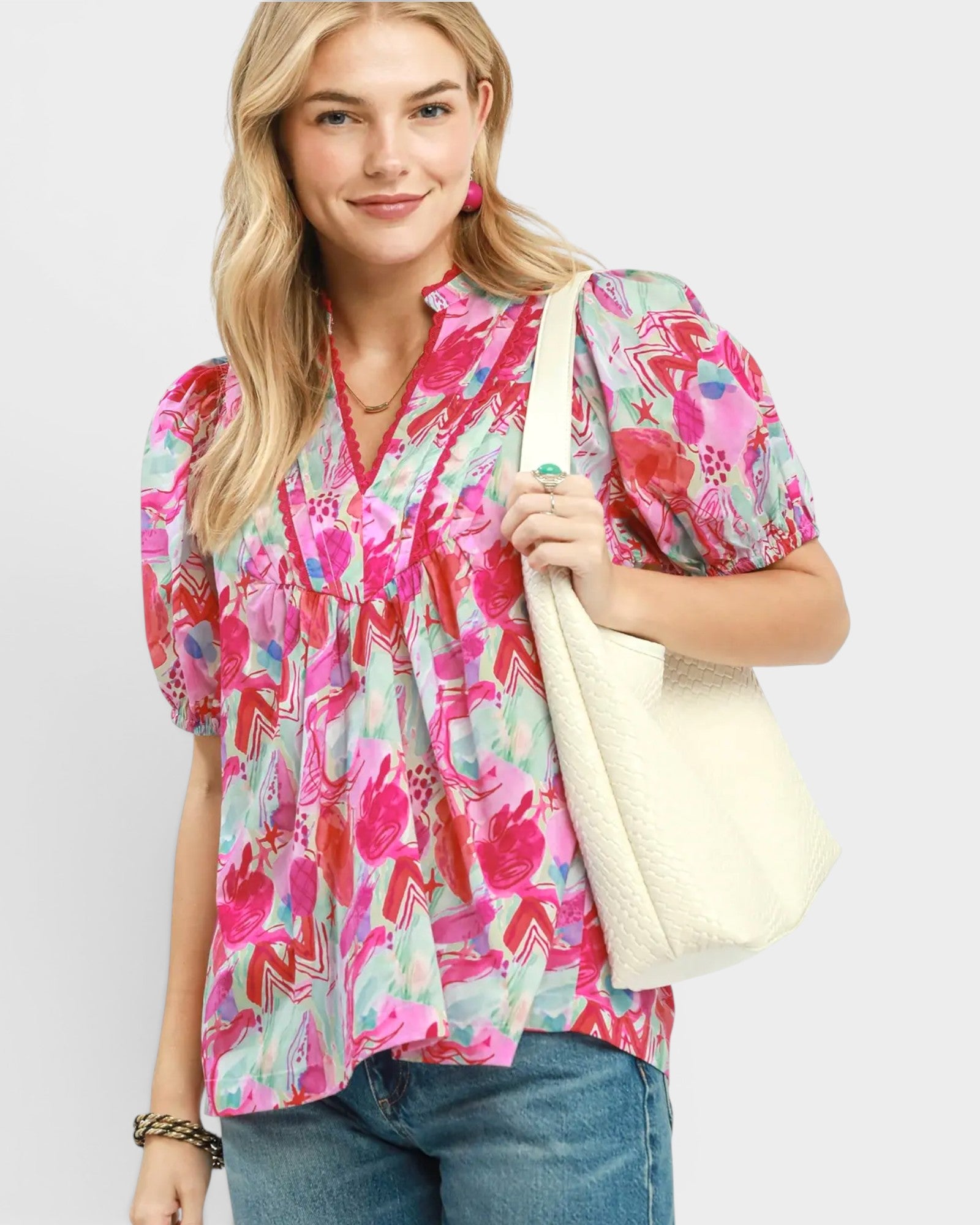 Woman wearing a colorful patterned blouse holding a white tote bag on a plain background