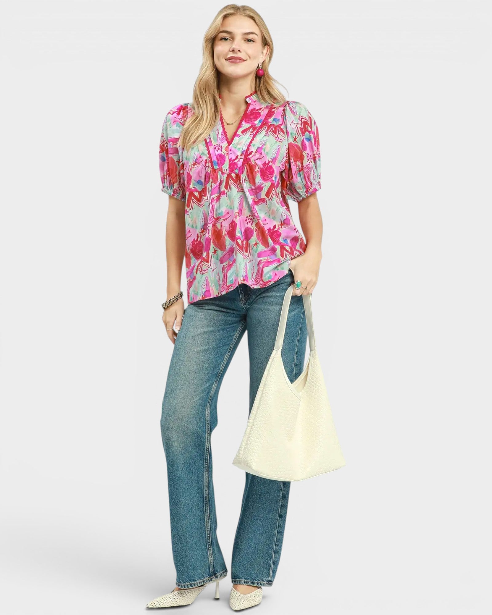 Woman wearing a colorful floral blouse and blue jeans, holding a white bag on a light gray background