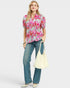 Woman wearing a colorful floral blouse and blue jeans, holding a white bag on a light gray background