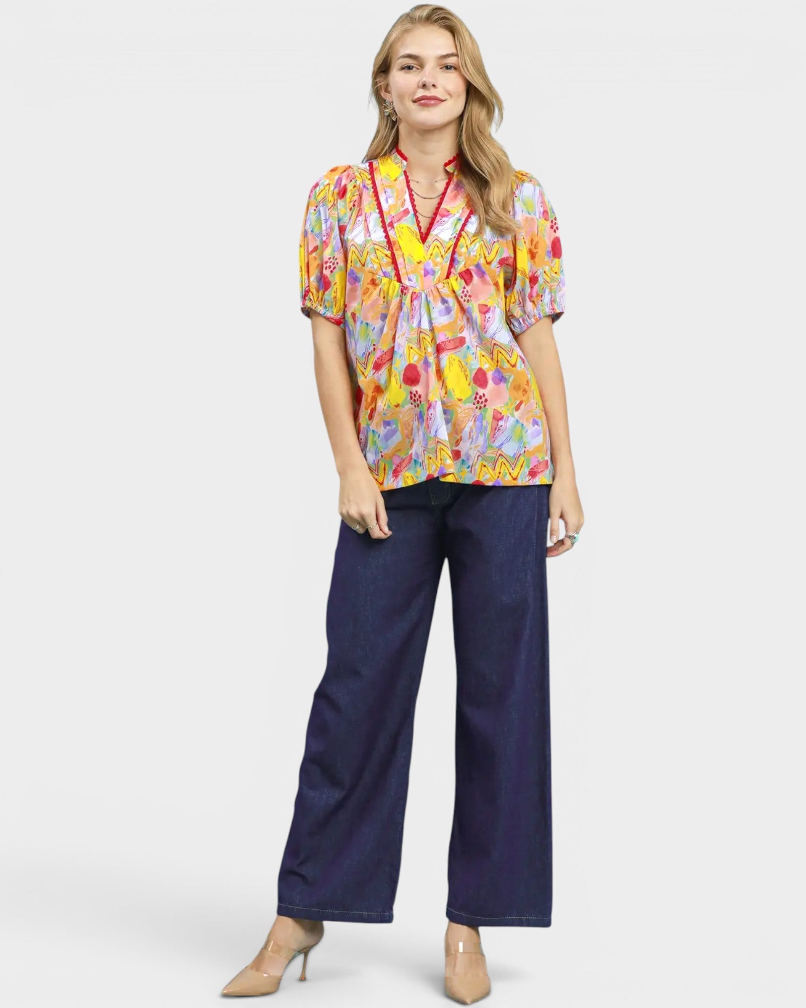 Woman wearing a colorful floral blouse and navy pants on a white background