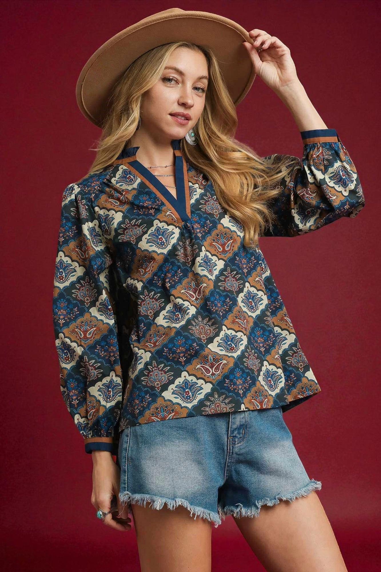 Woman wearing a patterned blouse and denim shorts against a red background