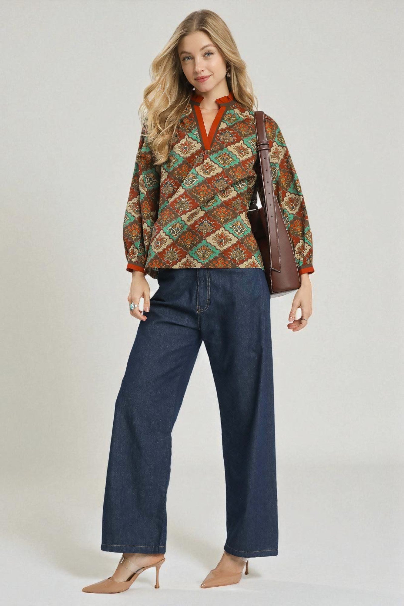 Woman wearing a patterned top and blue pants with a brown bag on a white background