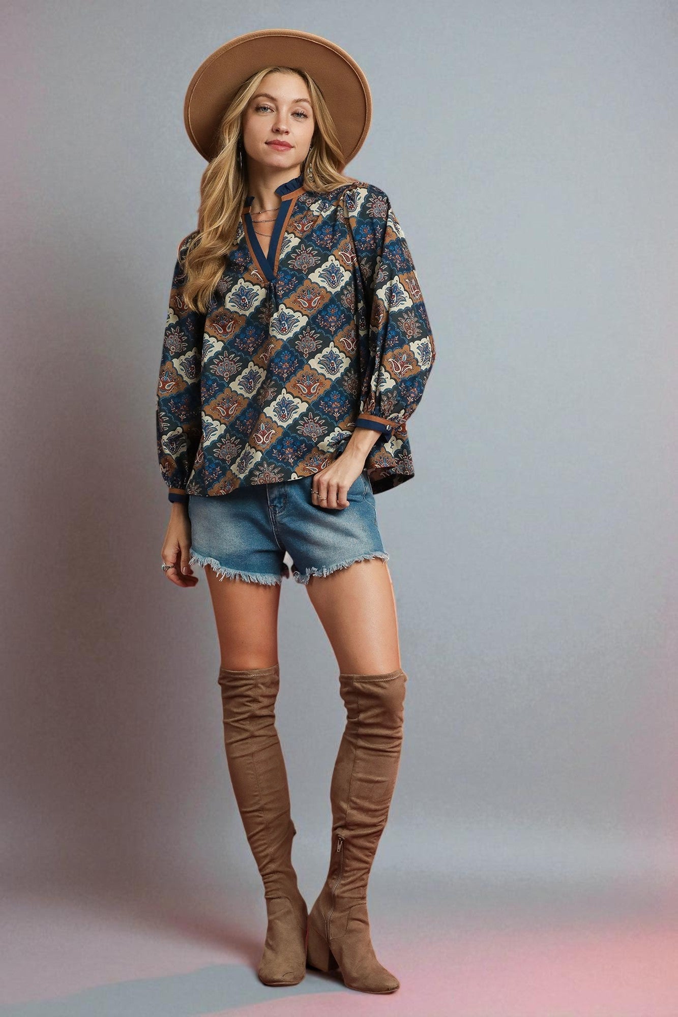 Woman wearing a patterned shirt, denim shorts, and brown knee-high boots against a plain background