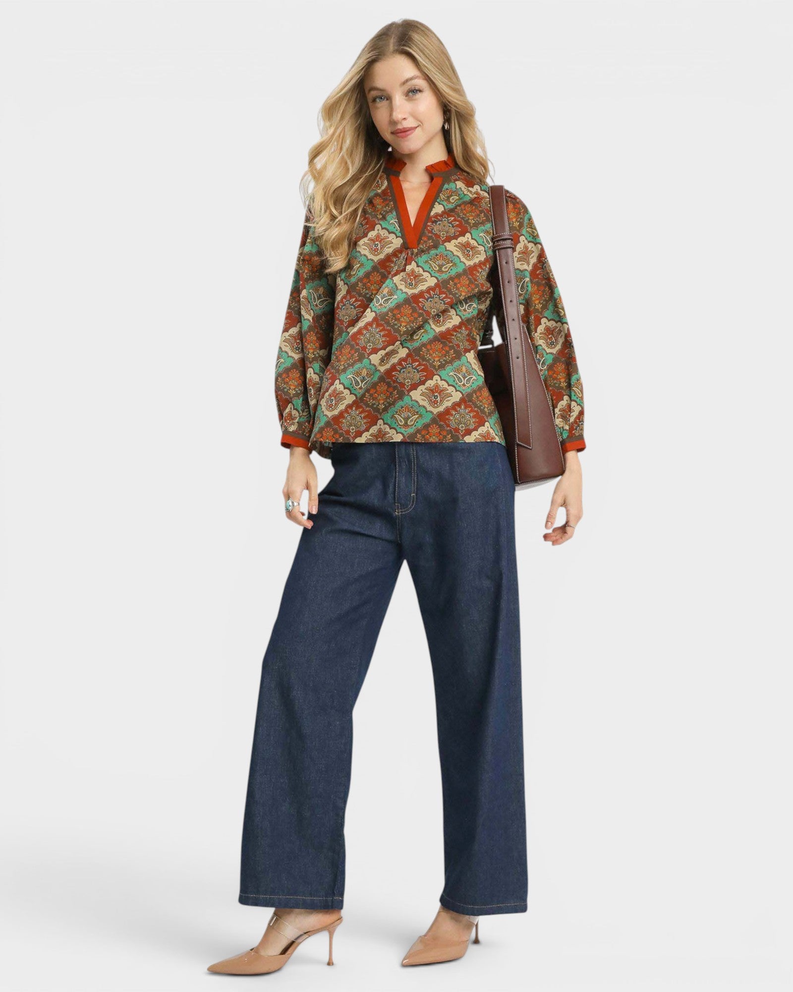 Woman wearing a patterned top and jeans with a brown bag on a white background