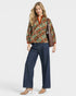 Woman wearing a patterned top and jeans with a brown bag on a white background