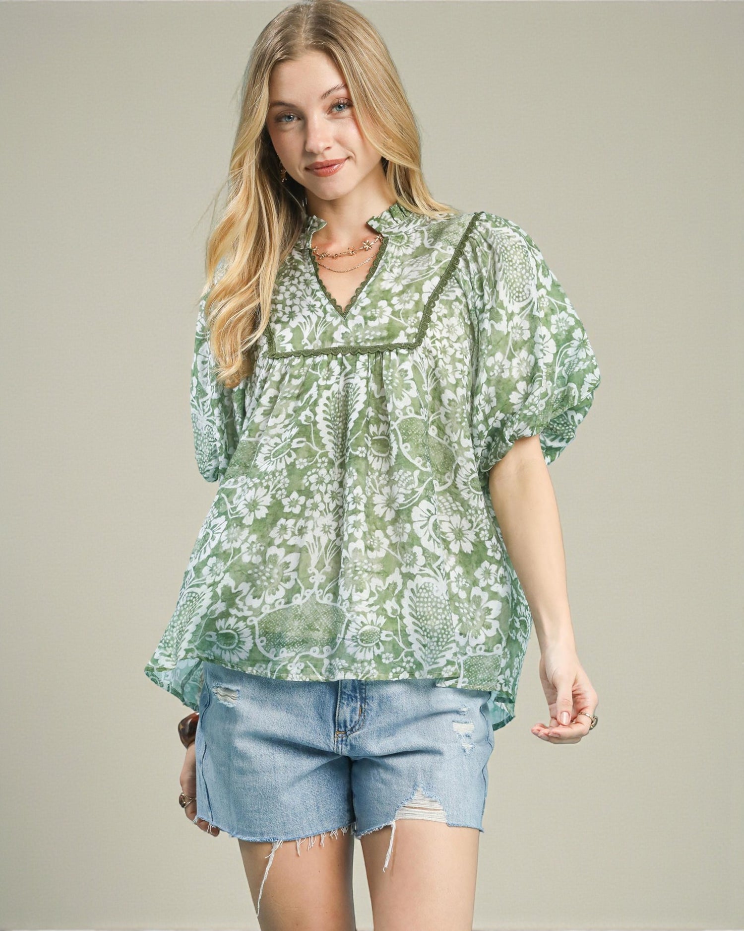 Woman wearing a green floral blouse and denim shorts on a plain background