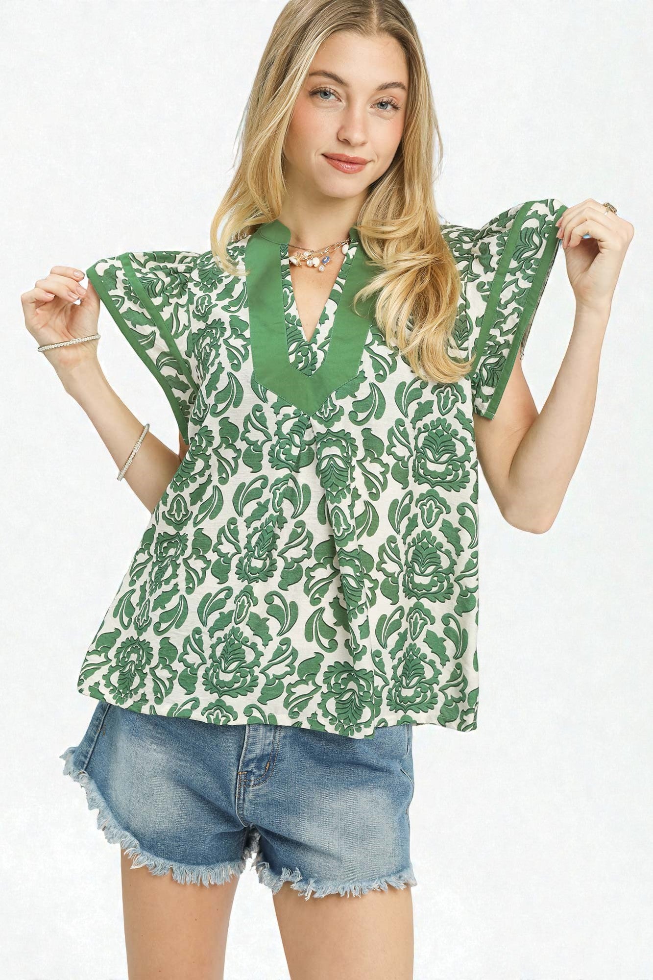 Woman wearing a green floral blouse and denim shorts on a white background