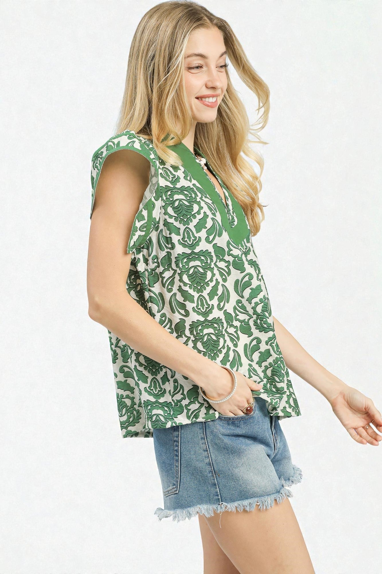 Woman wearing a green floral sleeveless top and denim shorts on a white background