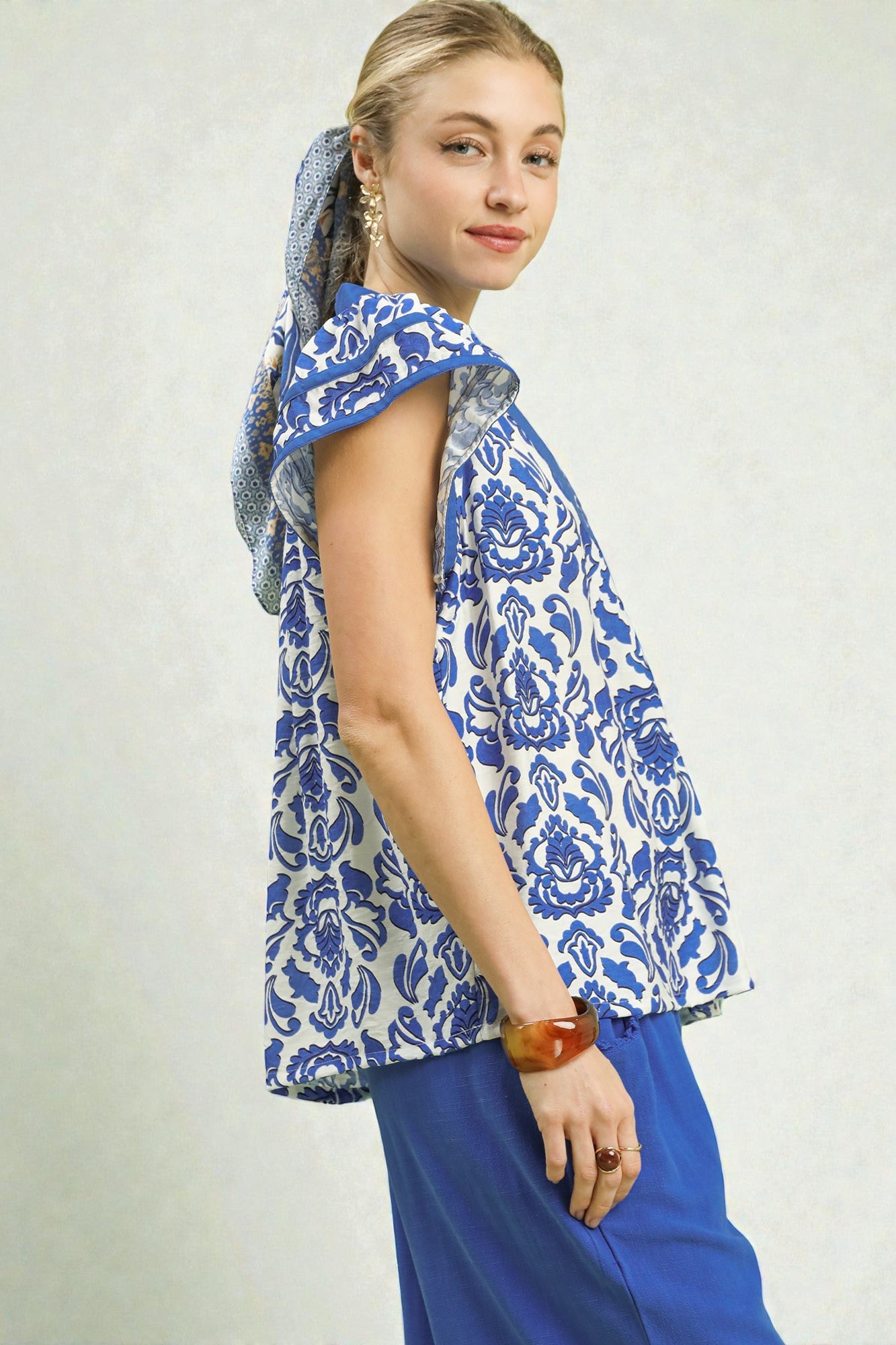 Woman wearing a blue and white patterned sleeveless top with a hood on a plain background