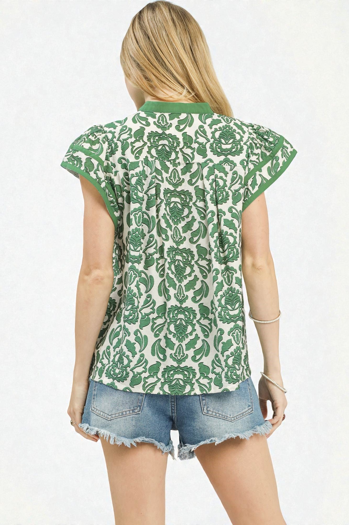 Woman wearing a green and white patterned sleeveless top with denim shorts on a white background