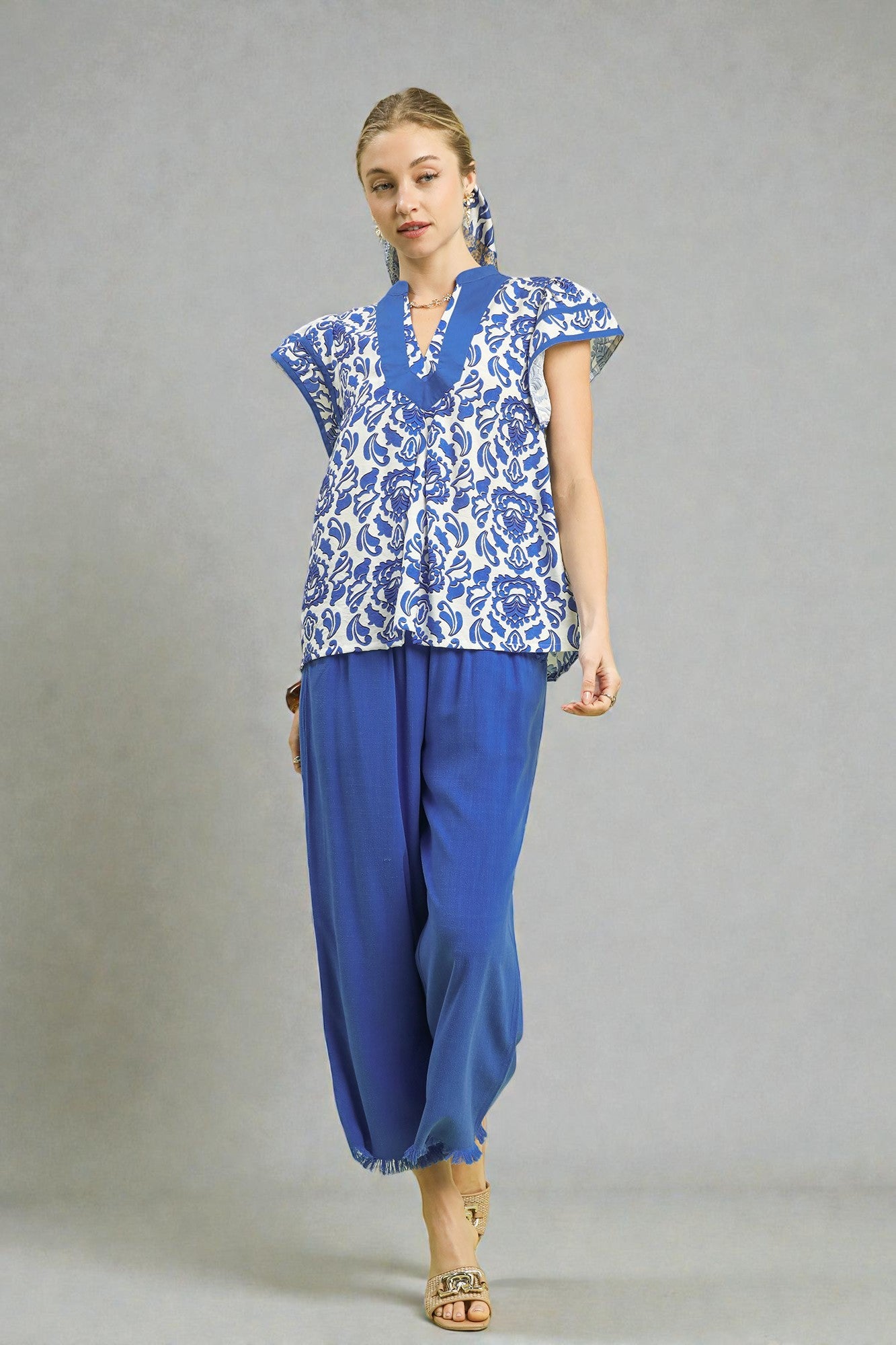 Woman wearing a blue patterned top and blue pants on a gray background