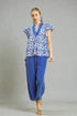 Woman wearing a blue patterned top and blue pants on a gray background