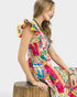 Young girl wearing a colorful dress sitting on a wooden stool against a white background