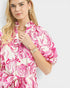 Woman wearing a pink and white patterned dress on a plain background