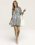 Woman wearing a colorful floral dress holding a white bag on a light background