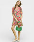 Woman wearing a colorful floral dress holding a green handbag on a white background
