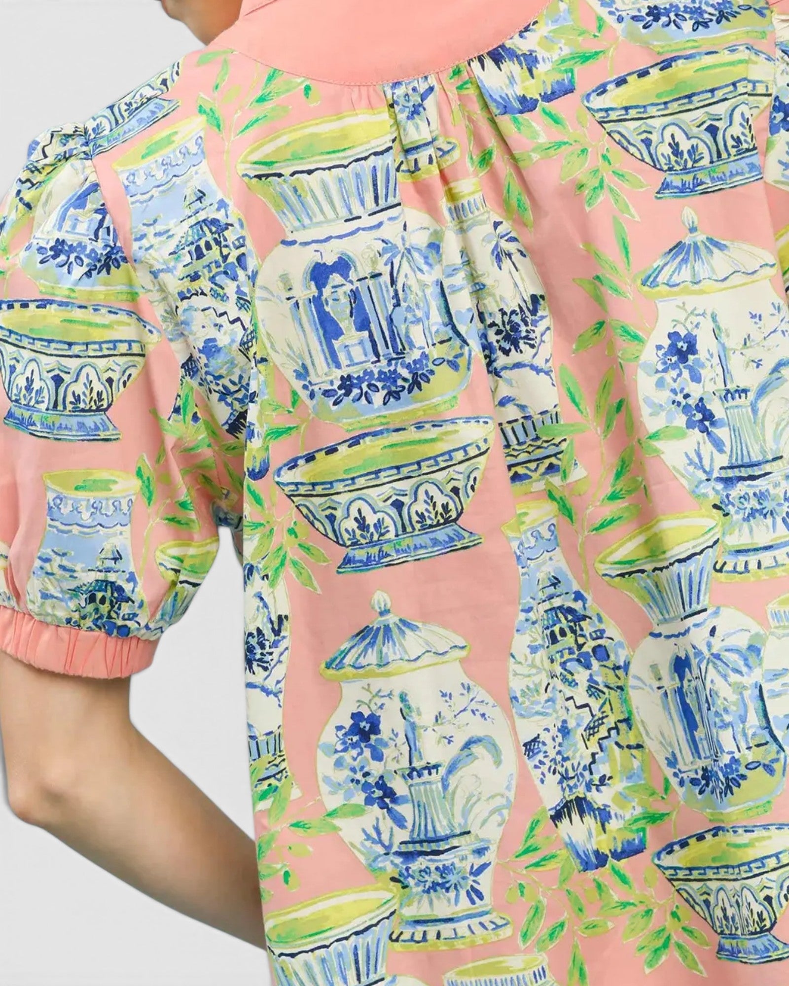 Person wearing a blouse with a blue and green vase pattern on a pink background