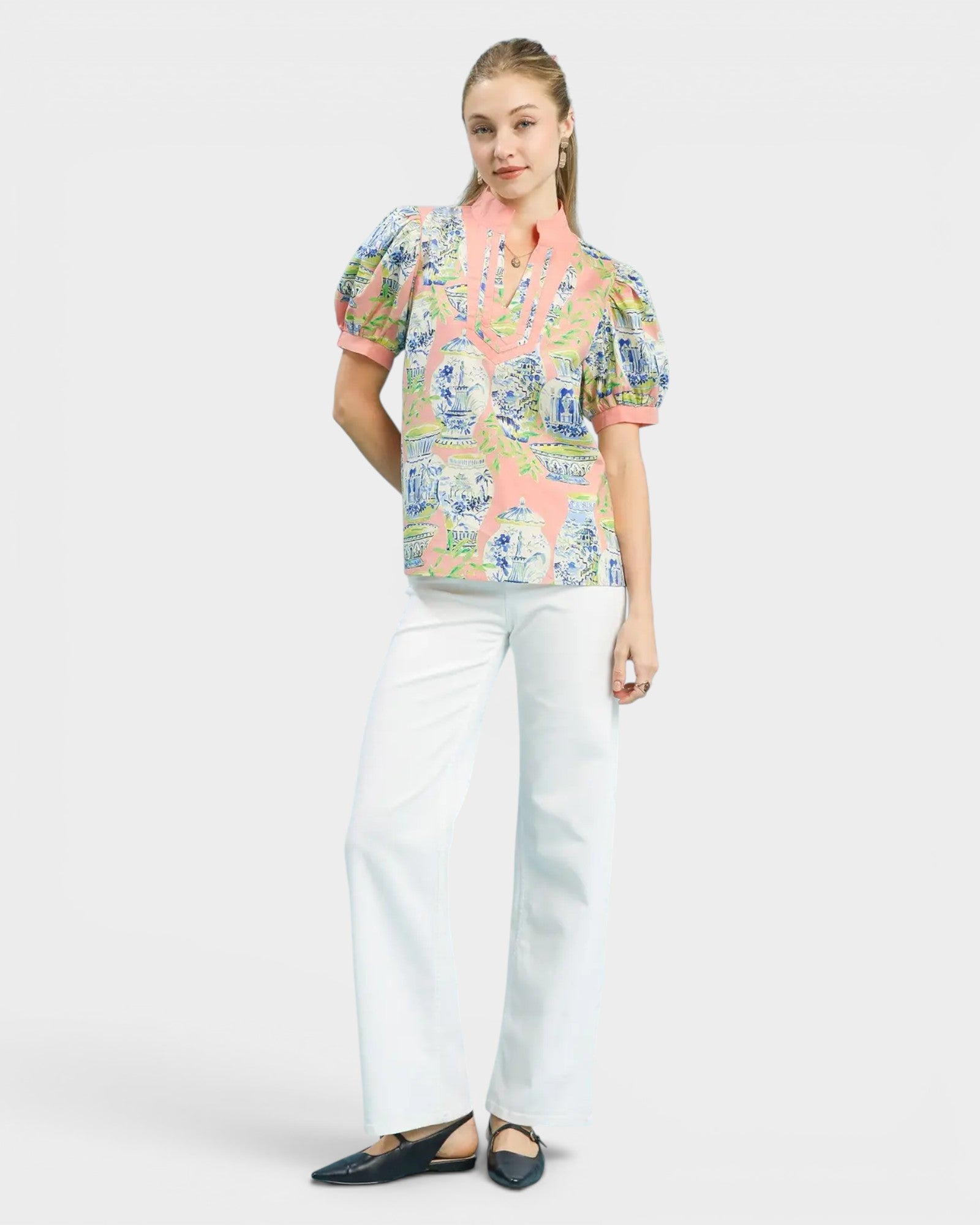 Woman wearing a colorful patterned blouse and white pants on a white background