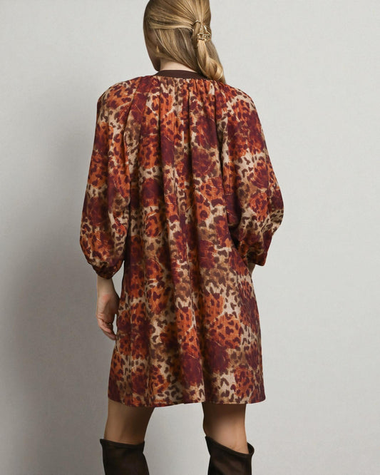 Person wearing a patterned dress with long sleeves on a plain background