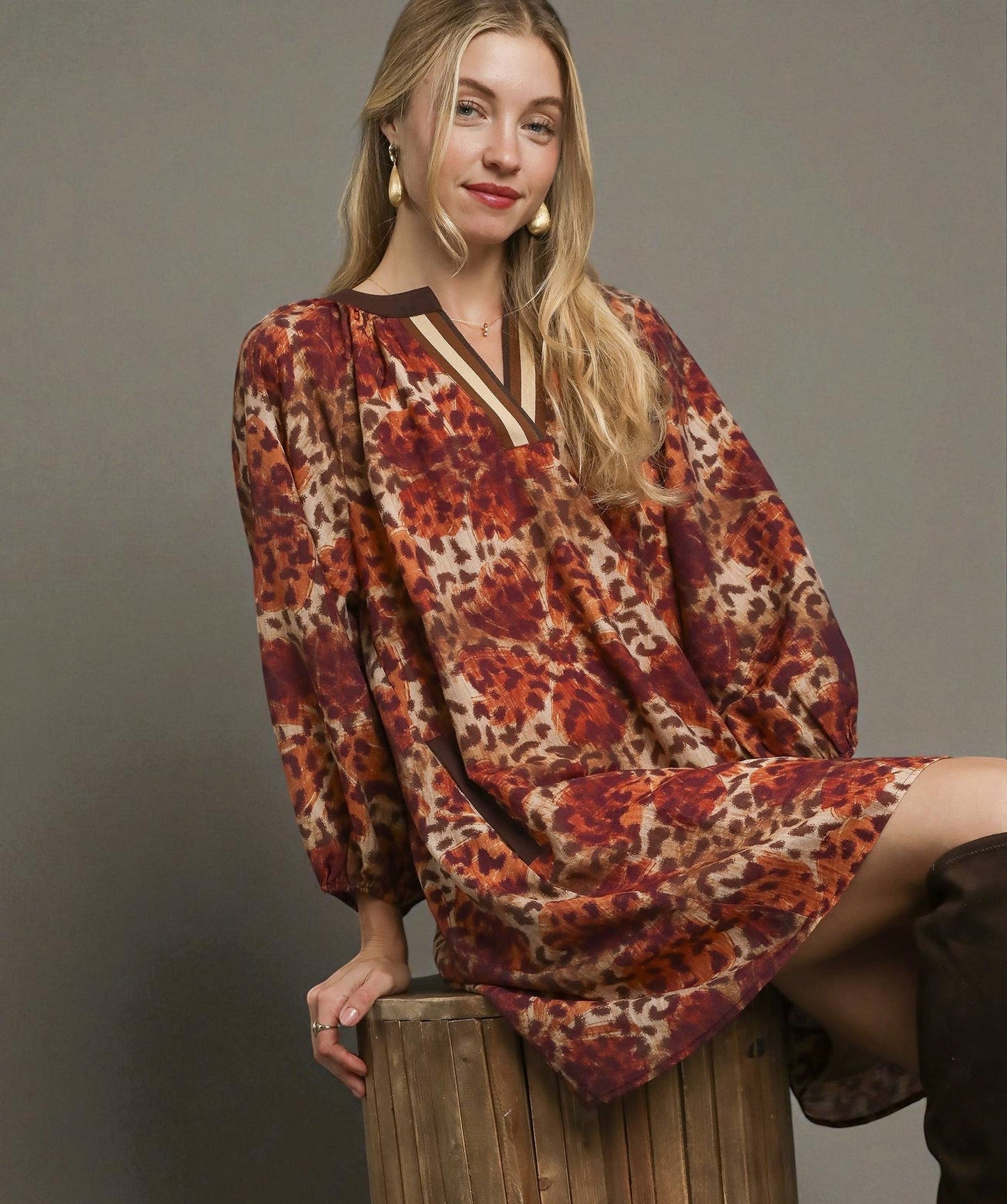 Woman wearing a patterned dress sitting on a wooden stool against a plain background