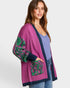 Woman wearing a purple cardigan with green patterns on a white background