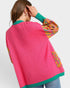 Person wearing a colorful sweater with pink back and multicolor sleeves on a light gray background