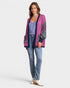 Woman wearing a pink cardigan with green patterns, blue jeans, and white boots on a white background