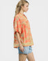 Woman wearing a coral floral blouse and denim shorts on a white background