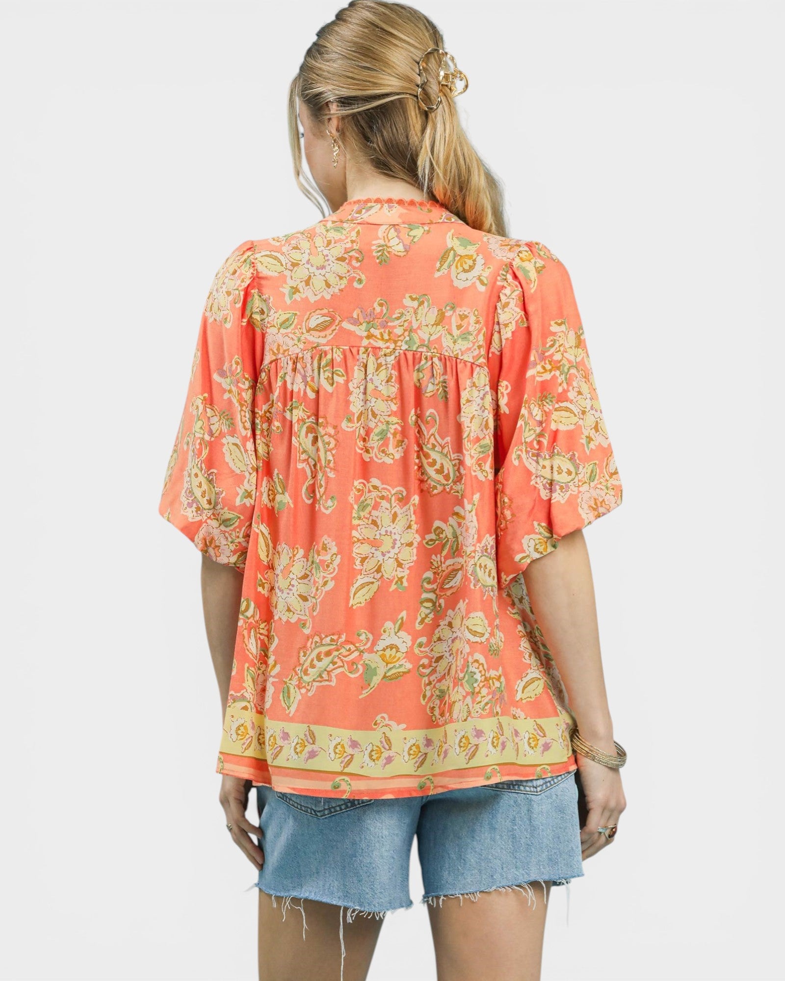 Woman wearing a coral floral blouse with denim shorts on a white background