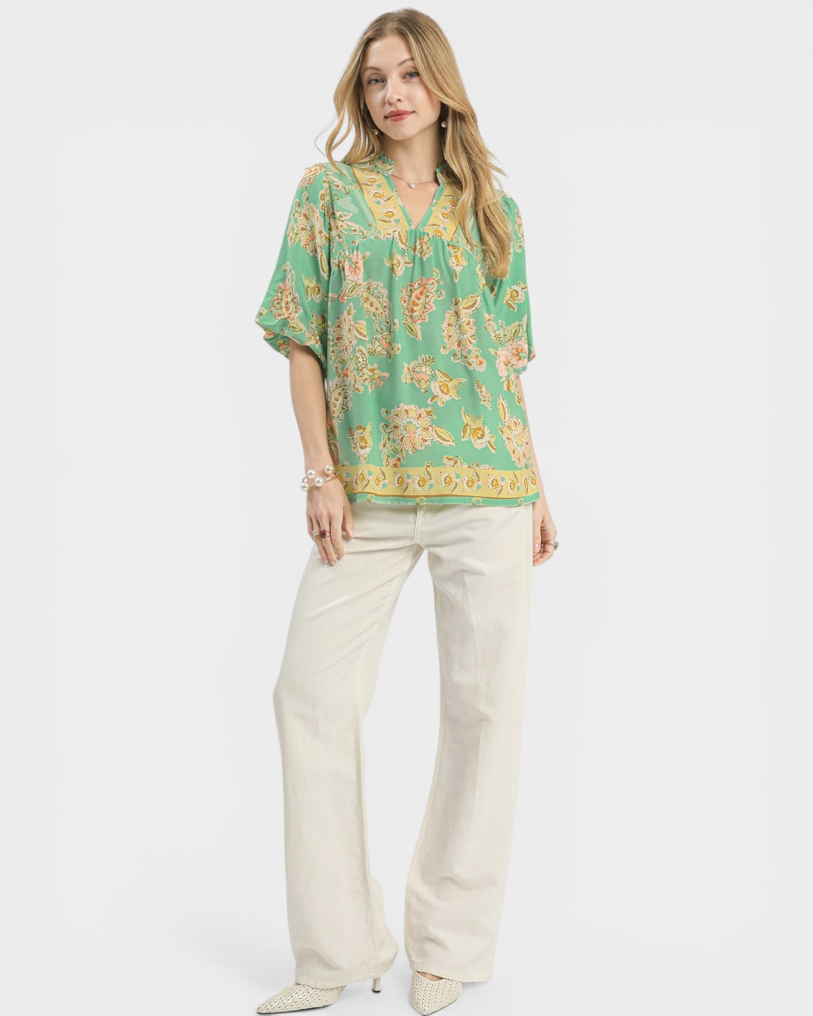 Woman wearing a green floral blouse and white pants on a white background
