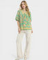 Woman wearing a green floral blouse and white pants on a white background