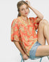 Woman wearing a floral blouse and denim shorts sitting on a chair against a plain background
